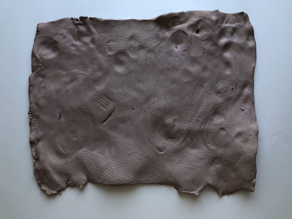 A rectangular raw ceramic slab containing various impressions along its surface and edges.