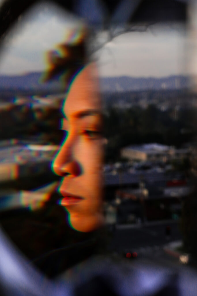 Photograph of a cityscape with a fragmented reflection of a person’s profile overtaking the center of the composition.
